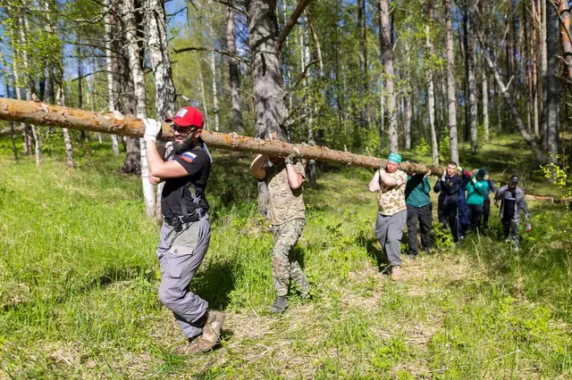 Группа участников несёт бревно через лес во время учебной подготовки